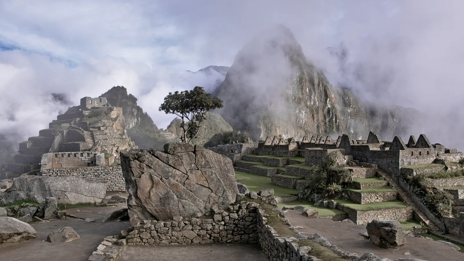 Ruinas de Machu Picchu con terrazas y el Huayna Picchu cubierto de nubes al fondo